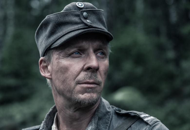 Kuvassa on Eero Aho Tuntemattomattoman sotilaan kasvokuvassa, jossa hänellä on sotilassuikka päässään.