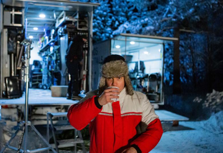 Kuvassa on Jarkko Lahti, joka esittää metsuria. Hän on juomassa pahvimukista kahvia.  Hänellä on puna-harmaa toppatakki päällään ja taustalla näkyy lumisessa metsässä 