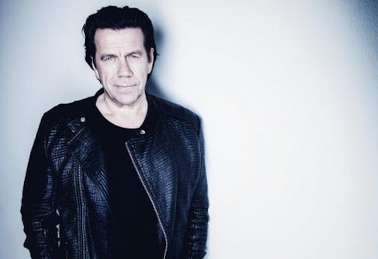 Kuvassa on Mikko Kuustonen puoliksi vaalean ja tumman tausta edessä.  Hänellä on musta nahkatakki päällään.