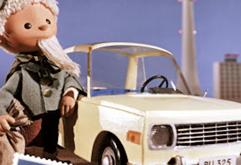 Kuvassa on Nukkumatti harmaassa takissa nojaamassa vaaleaan itäsaksalaisen Wartburg-auton vieressä.