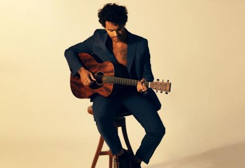 Kuvassa on Pete Parkkonen istumassa tuolilla ja soittamassa kitaraa.  Kuvan tausta on kellertävä.