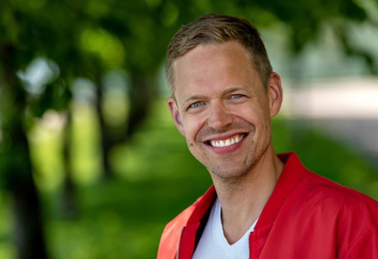 Kuvassa on kasvokuva Signmarkista ja taustalla on vihreitä lehtipuita.