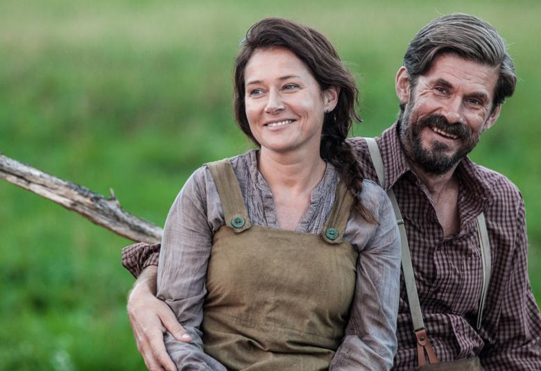 Kuvassa ovat Sidse Knudsen ja Tommi Korpela, jotka istuvat ja nojaavat toisiinsa. Taustalla on vihreää ruohoa.