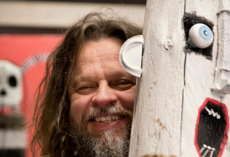 Kuvassa on Jori Kalliola, joka kurkistaa pölkkypääveistoksensa takaa. 