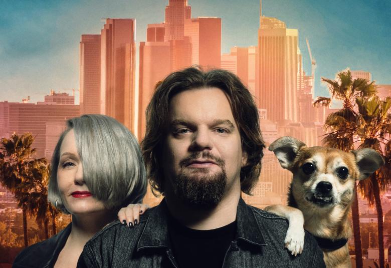 Kuvassa ovat Angela ja Ismo Leikola puolivartalokuvassa ja heidän takanaan on vaalean ruskeita pilvenpiirtäjiä sekä sinistä taivasta.