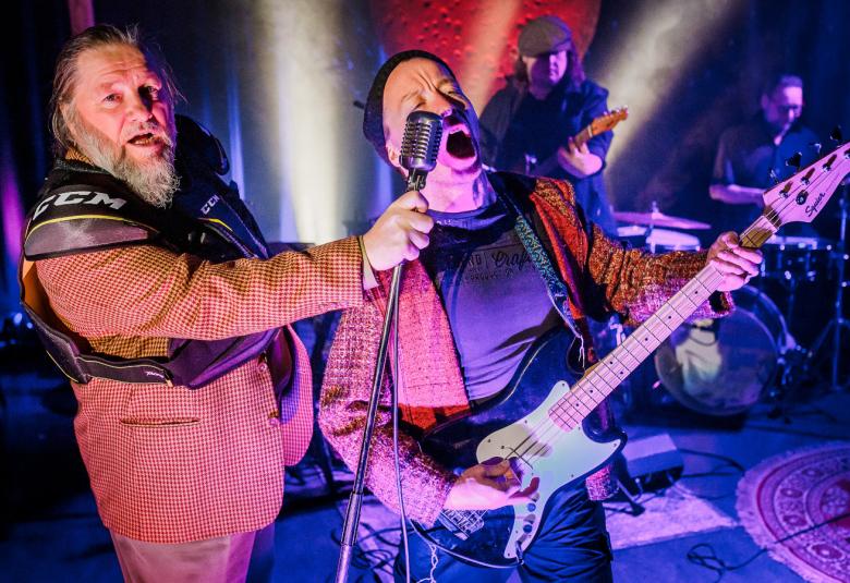 Kuvassa ovat Don Ookoo ja Tohkane laulamassa mikin ääressä takanaan tummahko näyttämö, jossa on valoja. Tokanella on kitara kädessään.