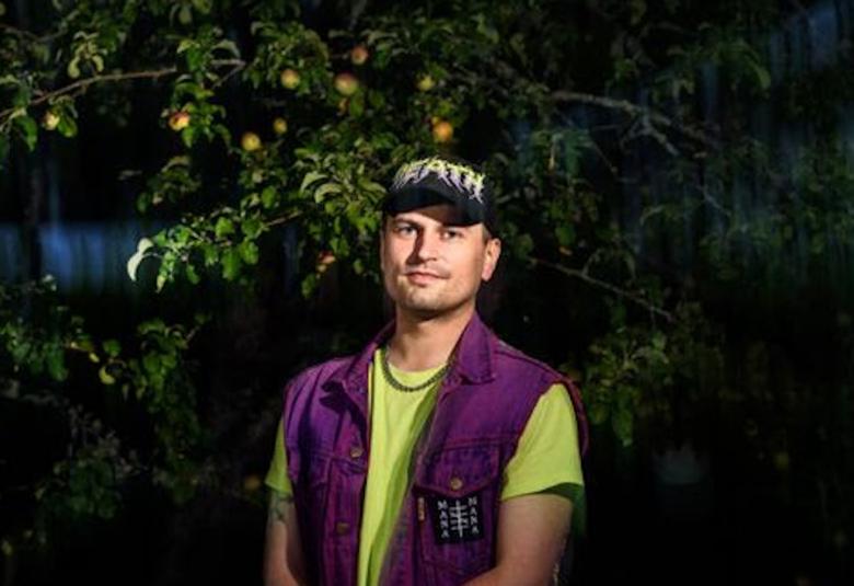 Kuvassa on Joel Slotte vihreässä t-paidassa ja vieletissä liivissä. Takana on omenapuu, jossa on omenoita.