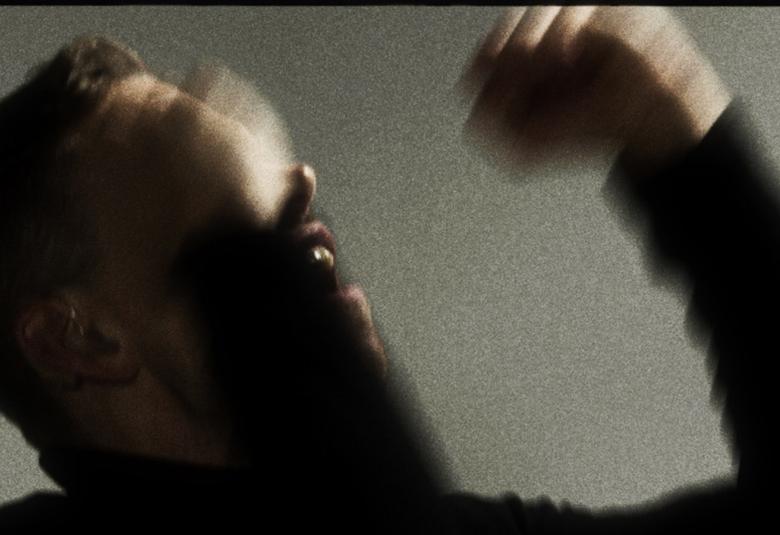 Kuvassa on Signmarkin kasvot ja käsi  ylhäällä sivuttain himmeästi tummalla.