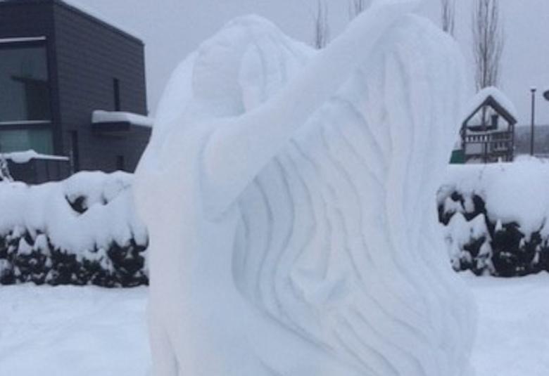 Kuvassa on voittanut lumiveistos Ilona, jossa on naishahmo kiipeämässä koverruskuvioiseen seinämään.