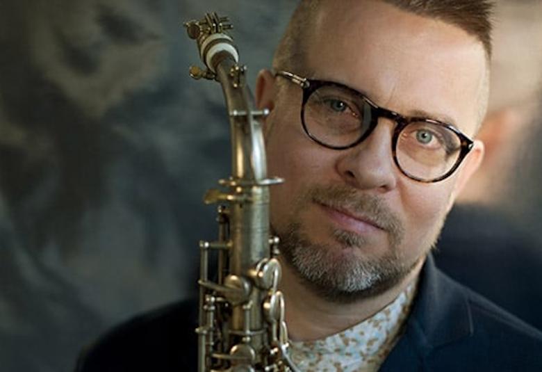 Kuvassa on Jukka Perkon kasvokuva ja hänellä on edessään saksofoni.