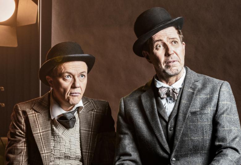 Kuvassa ovat Martti Suosalo ja Mika Nuojua ovat istumassa ruudullisissa pikkutakeissa ja knalleissa.  