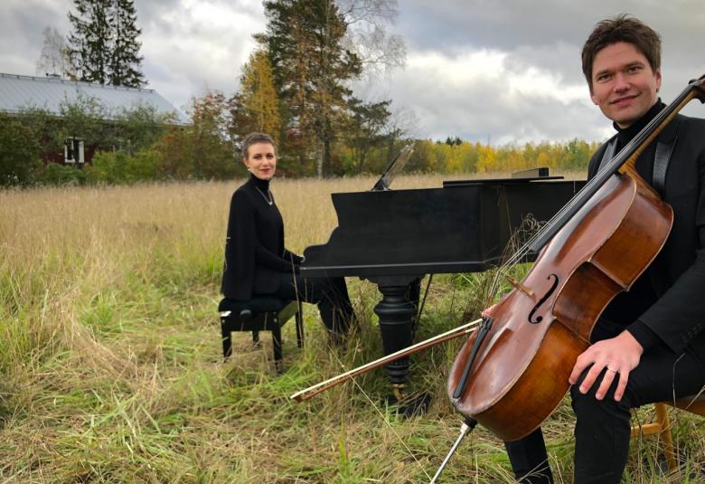 Azezian taaempana soittamassa flyygeliä heinäpellolla. Taustalla kauempana on punainen talo.