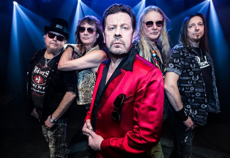 Kuvassa on Popeda-yhtye sinisävyisessä ympäristössä ja keskimmäisenä on pate Mustajärvi punaisessa takissa.