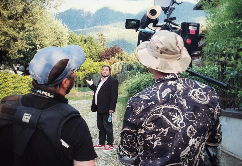 Kuvassa on kaksi kuvaajaa selin ja heidän keskeltään kauempaa näkyy Joonas Berghåll seisomassa. Kuva on otettu ulkona.