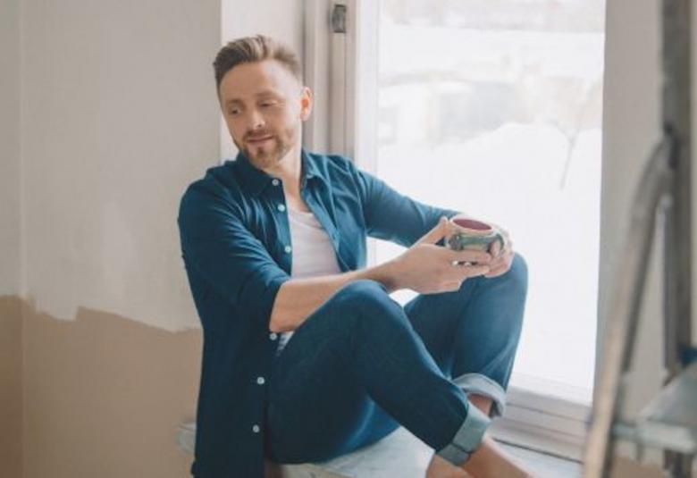 Kuvassa on Reino Nordin istumassa ikkunalaudalla huoneessa, jossa on remontti ja seinät on puoliksi maalattu vaaleahkolla värillä.