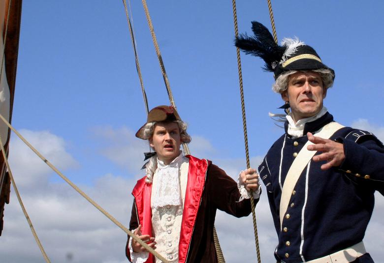 Kuvassa on kaksi vanhanajan sotilaspuvuissa olevaa miestä, joilla on isot hatut päässään ja asetakit päällään.