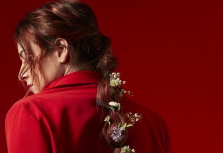 Kuvassa on Erin selin ja hänellä on punainen mekko päällään.  Hiukset ovat takaa poninhännällä ja siihen on kiedottu kukkia.