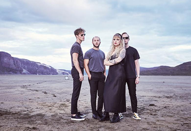  Kuvassa on Haloo Helsingin neljä jäsentä seisomassa hiekkaisessa maisemassa ja taustalla on isoja kallioita.