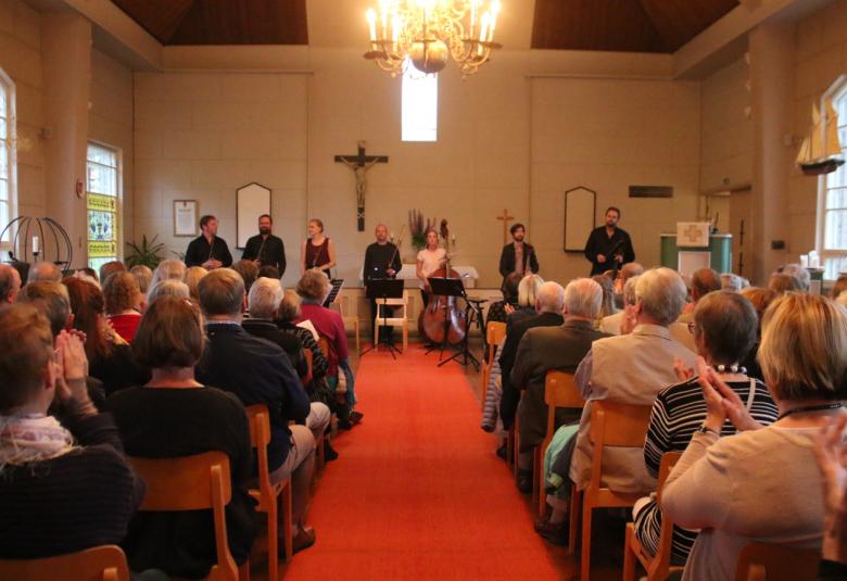 Kuvassa on konsertin päätös, jossa Klamilan kirkon etuosassa soittajat ottavat yleisön aplodeja vastaan.  Etualalla on yleisöä ja keskellä on käytävä.