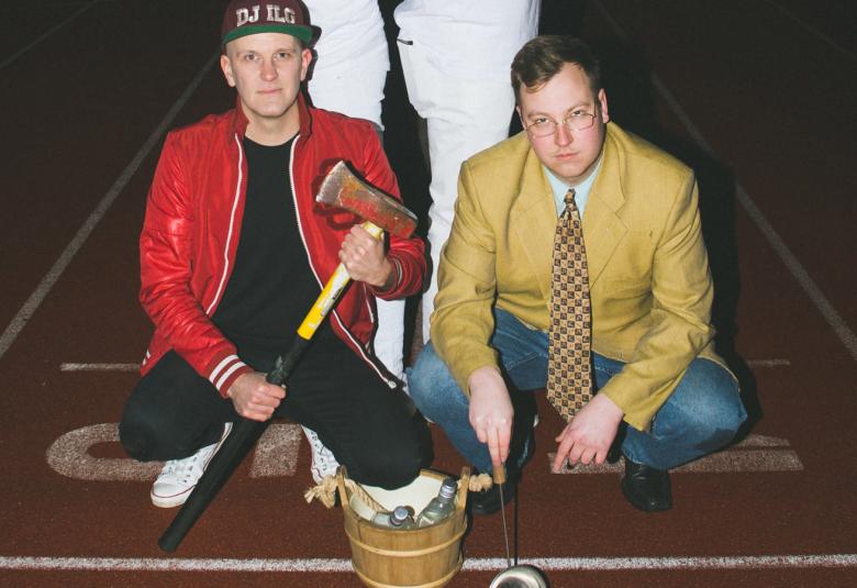 Kuvassa ovat Mika kyykyssö mustassa nahkatakissa kirves kädessään ja Samuli istumassa lattialla kellertävässä pikkutakissa. 