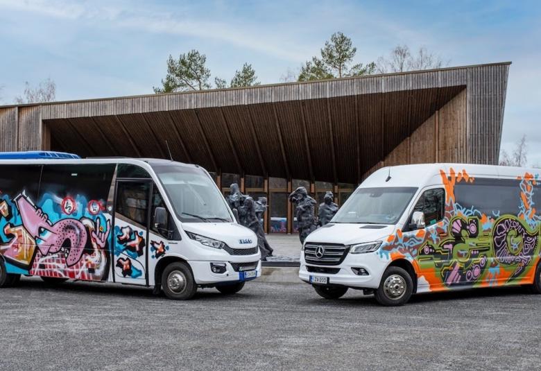 Kuvassa on kaksi pikkubussia, jotka ovat vinosti nokat toisiaan kohti.  Bussien kyljissä on graffiteja.