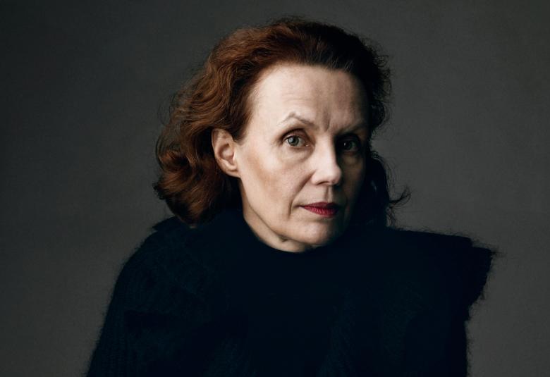 Kuvassa on Kaija Saariaho puolivartalokuvassa tummahkolla taustalla mustassa puserossa.