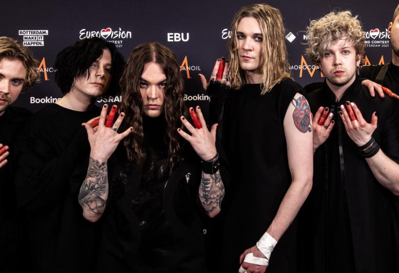 Kuvassa on Blind Channel yhtye mustissa t-paidoissa ja yhtyeen jäsenet näyttävät sormiaan, joista keskisormi on punainen. Taustalla seinässä näkyy logo Eurovision.