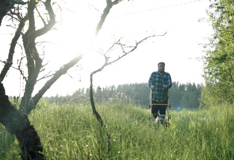 Kuvassa on Joonas Berghåll keskellä pitkää ruohikkoa ja vasemmalla on puun runkoja.