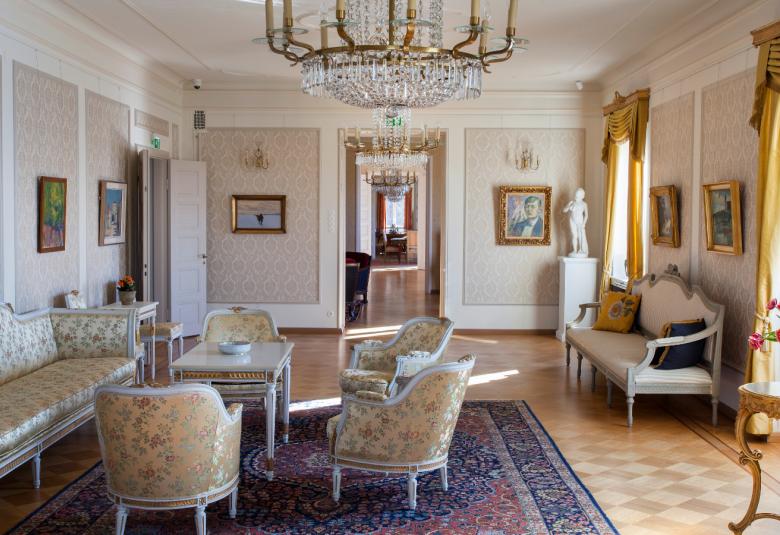 Kuvassa on Söderlångvikin kalustettu huone, jossa on vanhoja tyylikalusteita ja melko vaaleat värit.  Verhot ovat kullankeltaiset.