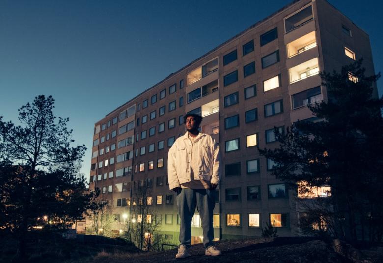 Kuvassa on Hassan Maikal seisomassa betonisen kerrostalon edessä.