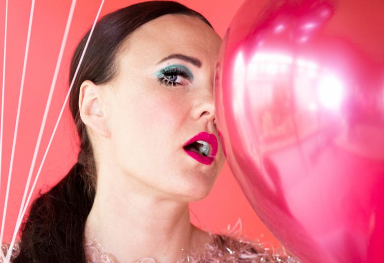 Kuvassa on Mira Luodin kasvot puoliksi vaalean punaisen ilmapallon takana.