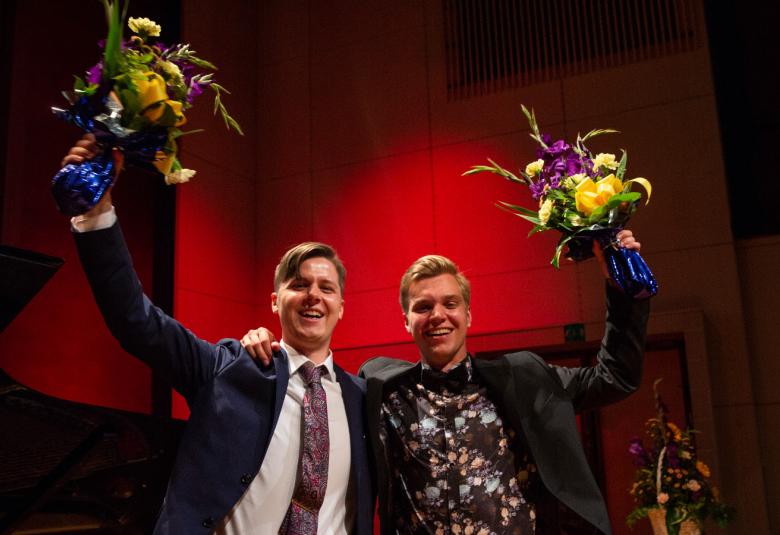 Kuvassa ovat Johan Krogius ja Jere Hölttä, jotka molemmat ovat nostaneet kukkakimput toisella kädellä ylös.