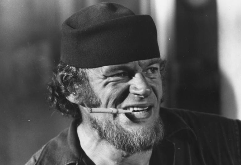 Kuvassa on Spede Härski Hartikaisena tupakka suussa. Kuva on kasvokuva ja musta-valkoinen.