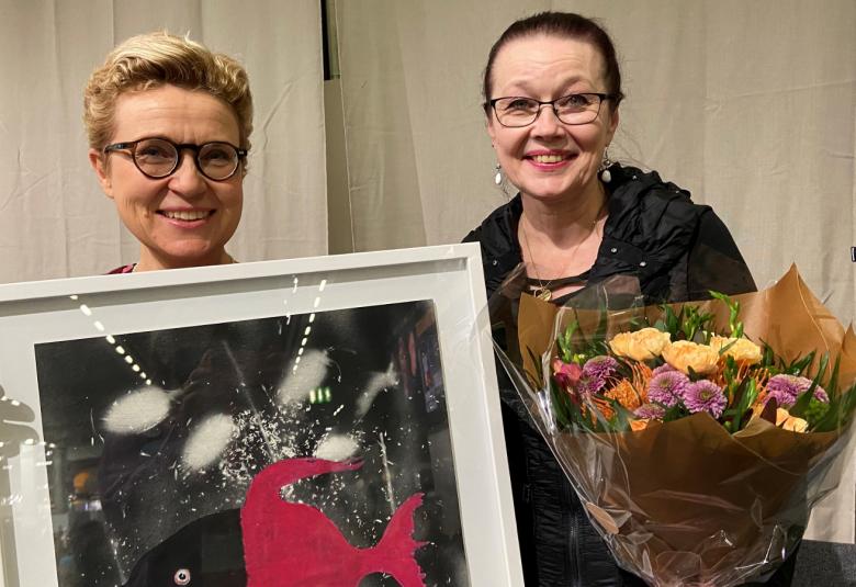 Kuvassa ovat Sirpa Kähkönen edesssään palkintotaulu ja Kini Laine kädessään värikäs, suuri kukkakimppu.