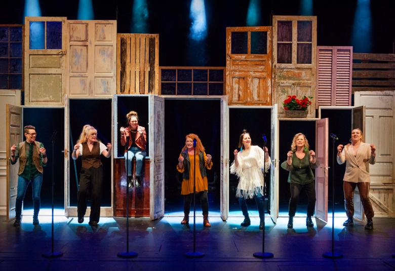 Kuvassa on näkymä näyttämöltä, jossa on ovia kahdessa kerroksessa ja jokaisella alla olevalla ovella on ovi auki ja jokaisessa oviaukossa on näyttelijä.