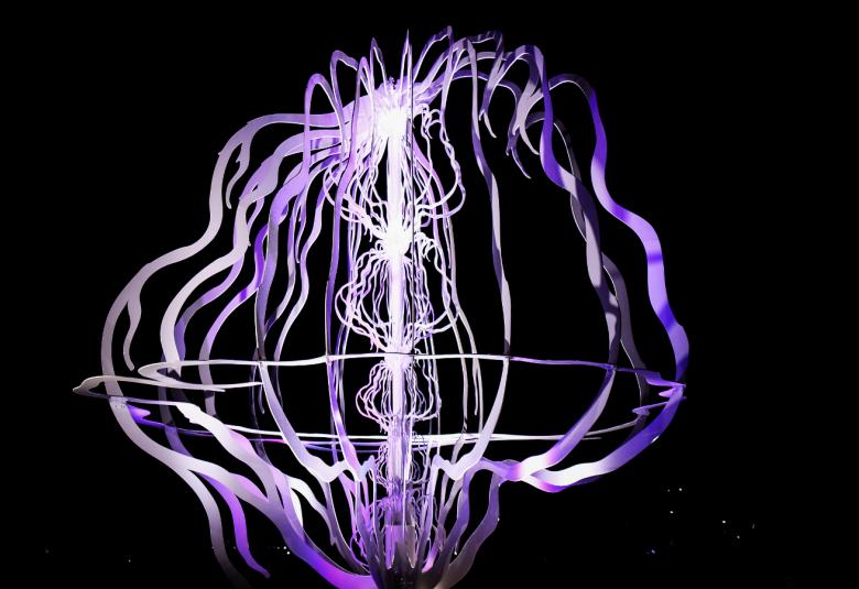 Kuvassa on tummalla taustalla on valkoisella ja lilalla valaistu nauhamainen tilataideteos.