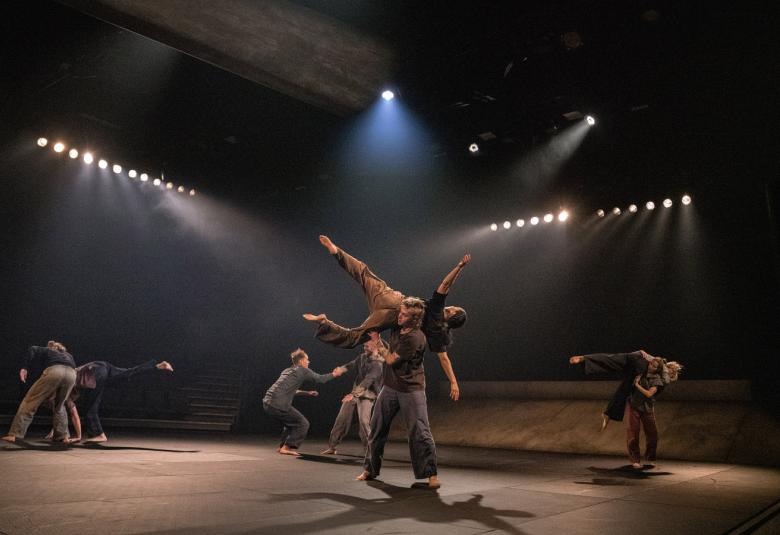 Kuvassa on näyttämöllä tanssijat ovat kasautuneena useaan suuntaan ulottuvaan muodostelmaan. Valot suuntautuvat neljään suuntaan kohti tanssijoita.