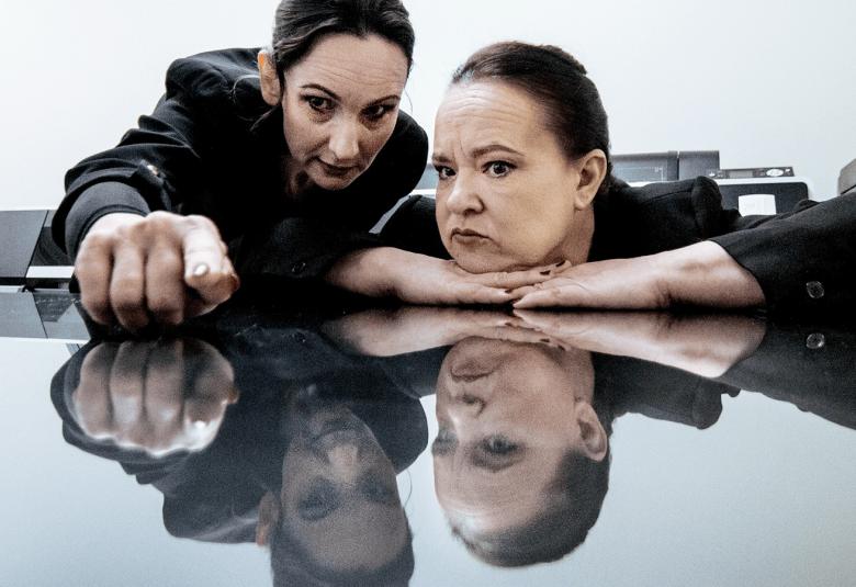 Kuvassa Miina Turunen ja Anna Veijalainen nojaavat ja katsovat kiiltävää pöydän pintaa.