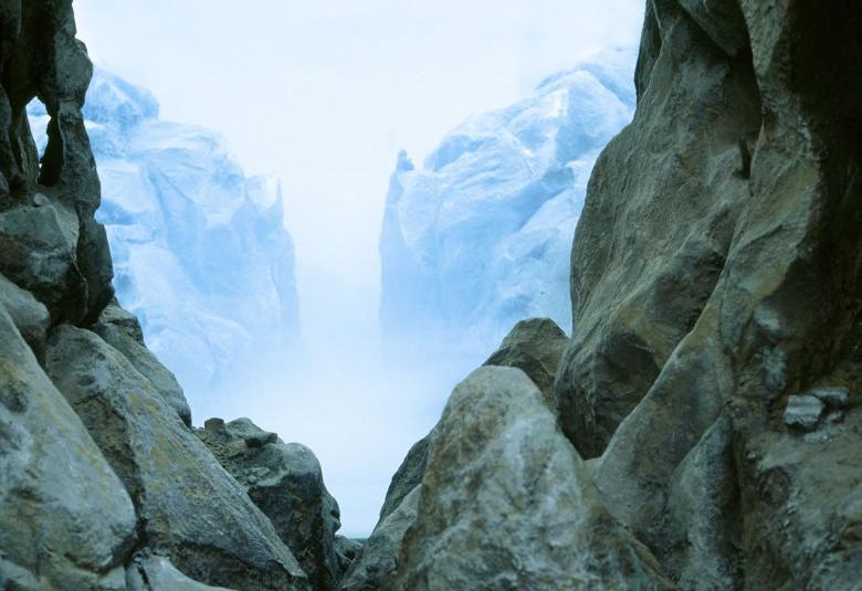 Kuvassa on Mariele Neudeckerin teos, jossa on kallioiden välissä oleva näkymä. Kuva on siniharmaan sävyinen.