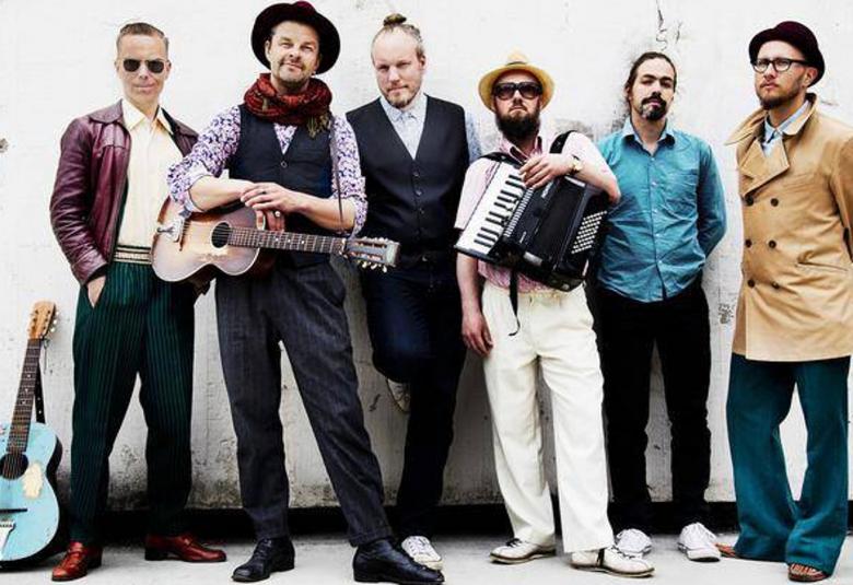 Kuvassa ovat Tuure Kilpeläinen ja Kaihon karavaanin viisi jäsentä. Kilpeläisellä on kitara kädessään ja yhdellä jäsenellä harmonikka sylissään.