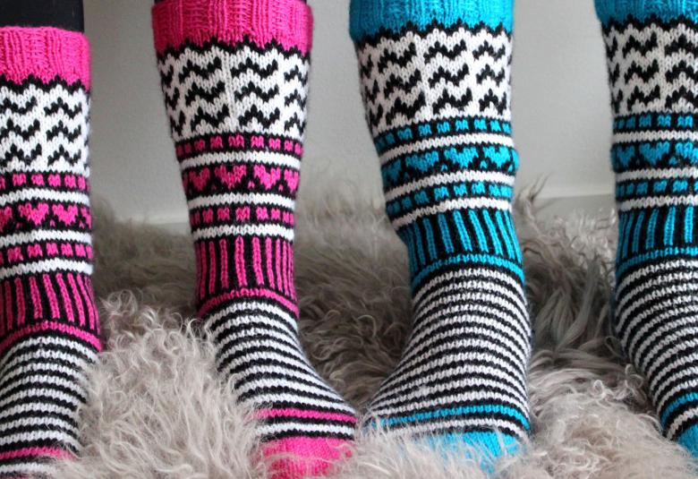 Kuvassa on kahdet jalat, joissa on raidalliset villasukat.  Toiset ovat aniliinin punaisella raidoitetut ja toiset turkoosilla raidoitetut sukat, joissa on lisäksi mustia ja valkoisia raitoja sekä pieniä kuvioita.