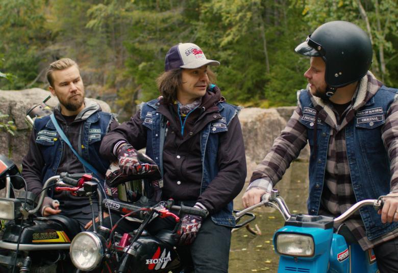 Kuvassa on mopojoengin kolme jäsentä ovat maastossa, metsän reunassa pysähtyneinä mopojen kanssa.