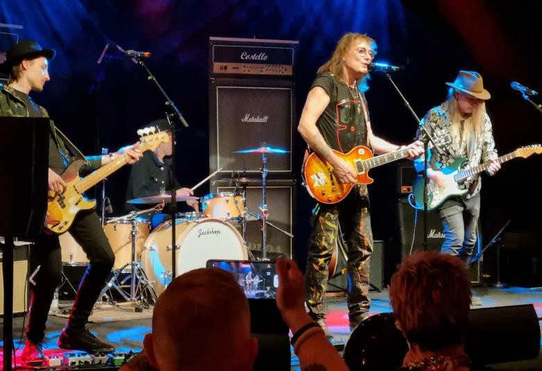 Kuvassa on kolme bändin soittajaa lavalla soittamassa kitaraa. 