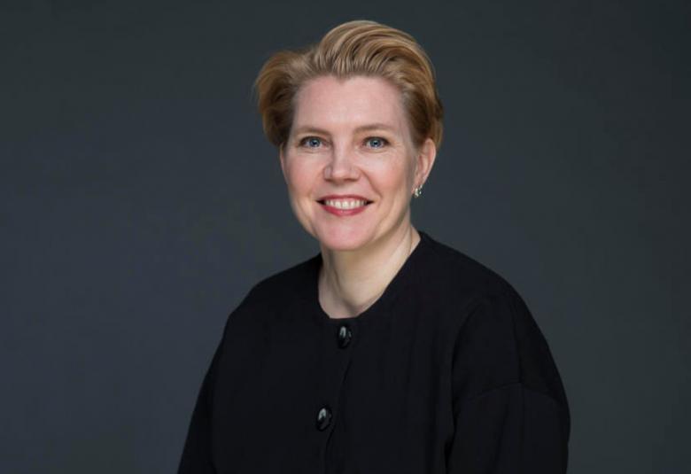 Kuvassa on Johanna Eiramo puolivartalokuvassa istumassa.  Hänellä on musta villatakki päällään. Kuvan tausta on harmaa.