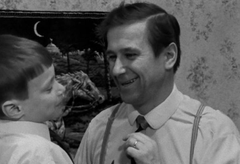 Kuvassa on Mikkko Niskanen yhdessä pojan kanssa kotona ja he juttelevat iloisesti vastatusten. Taustalla päiden takana on taulu. 