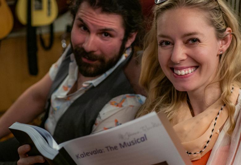 Kuvassa ovat musikaalin esiintyjät tummapartainen mies ja vaalea nainen. Heistä on kasvokuvat ja naisen kädessä ovat nuotit, joiden kannessa on teksti Kalevala the Musical. 