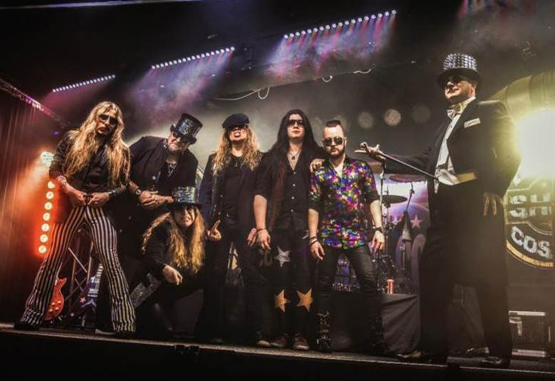 Kuvassa on seitsemän jäseninen bändi soittamassa lavalla, joka on tumma.