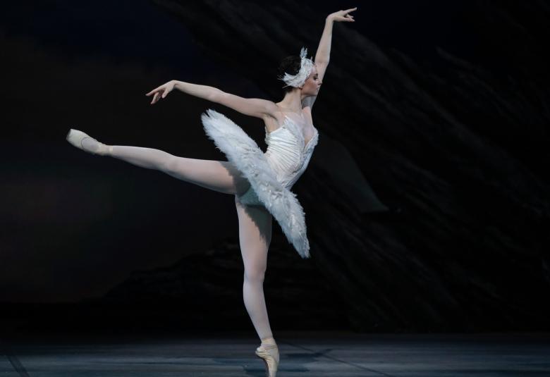 Kuvassa on Violetta Keller tanssimassa Joutsenlammessa sivukuvassa vasen käsi ojennettuna.  Tausta on tumma.