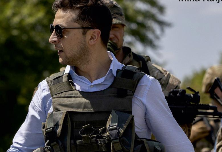 Kuvassa on Zelenski sotilasliivissä ja vaaleassa paidassa. Hänestä on sivukuva ja hänellä on aurinkolasit.