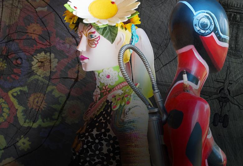 Kuvassa on vaalea mallinukke, jota on koristeltu ja päässä on iso valkoinen kukka keltaisella isolla mykiöllä. Vasemmalla on selin robotin näköinen toinen mallinukke, joka on maalattu sinisellä ja punaisella.